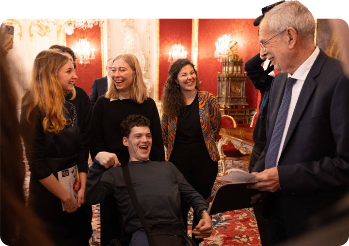 Wheelchair user and other participants engage in conversation with the Austrian president during a formal gathering in an ornate reception room.