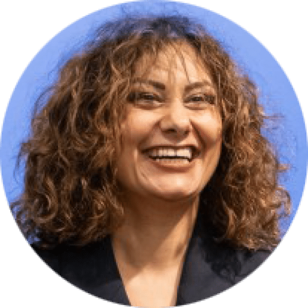 Headshot of a person with shoulder-length curly hair, wearing a dark blazer, against a light blue background.