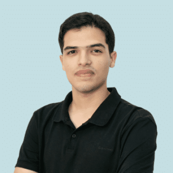 Head-and-shoulders portrait of a person wearing a black short-sleeve polo shirt, facing the camera against a light blue background. The person has short dark hair and is positioned slightly angled while looking toward the camera.