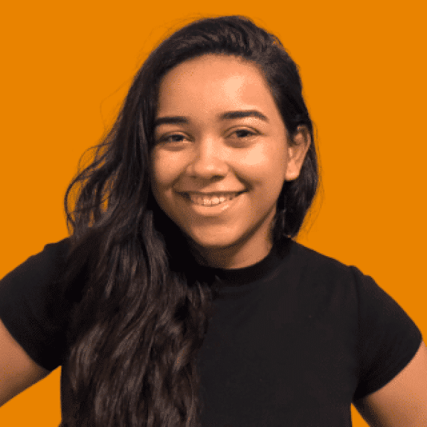 Head-and-shoulders portrait of a person with long dark hair, wearing a black short-sleeve top, facing the camera against a solid orange background. The image is evenly lit with a clean studio-style composition.