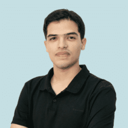 Head-and-shoulders portrait of a person wearing a black short-sleeve polo shirt, facing the camera against a light blue background. The person has short dark hair and is positioned slightly angled while looking toward the camera.