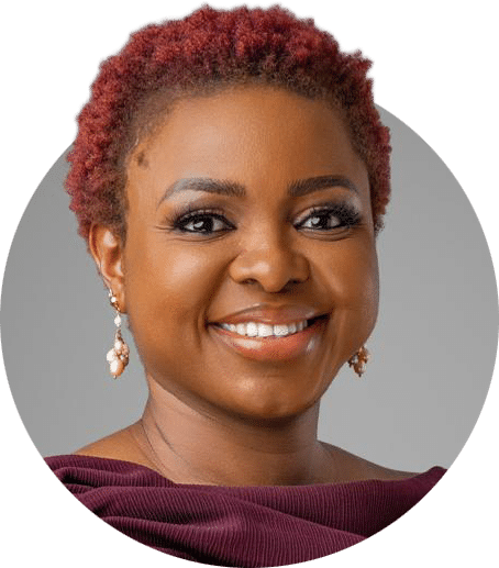 Headshot of a person with short textured hair, wearing drop earrings and a burgundy off-the-shoulder top, positioned against a light gray background.